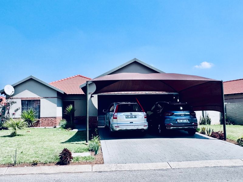 Front elevation of a single-story house featuring a paved driveway, a large shade cloth carport, and a well-maintained front garden.
