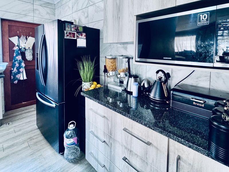 A functional kitchen featuring modern light wood-grain cabinetry, dark granite countertops, and a built-in microwave, complemented by marble-effect wall tiling.