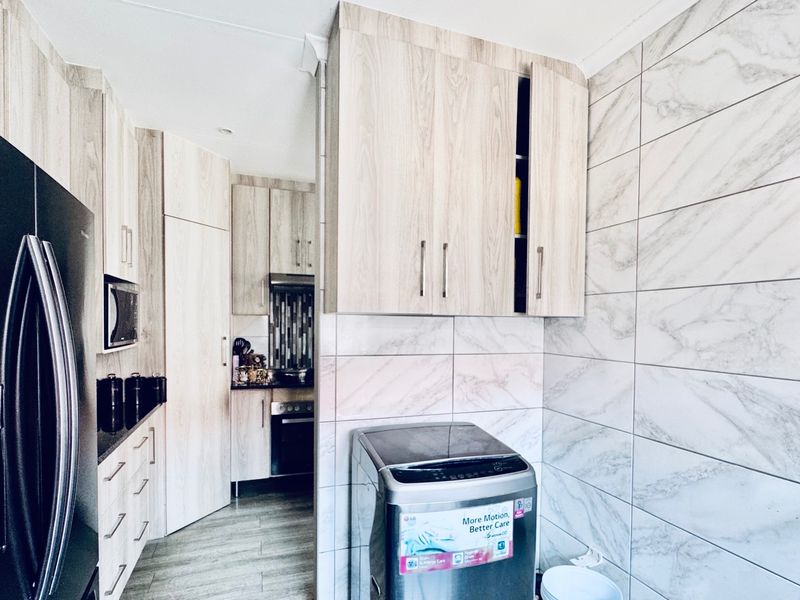 A modern laundry area featuring light wood-grain cabinetry, marble-effect wall tiling, and durable laminate flooring, providing a clean and functional utility space.