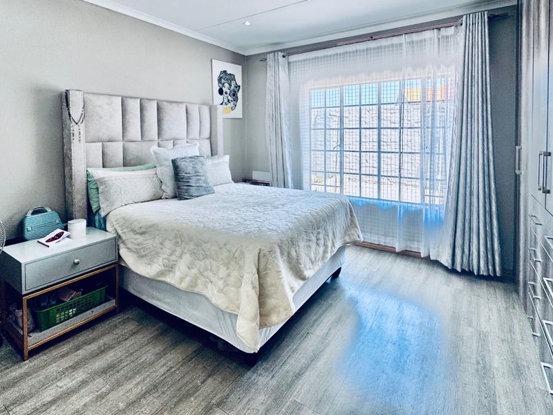 A well-maintained bedroom featuring modern laminate flooring, ample built-in cupboard storage, and large windows with curtain rails for natural light.