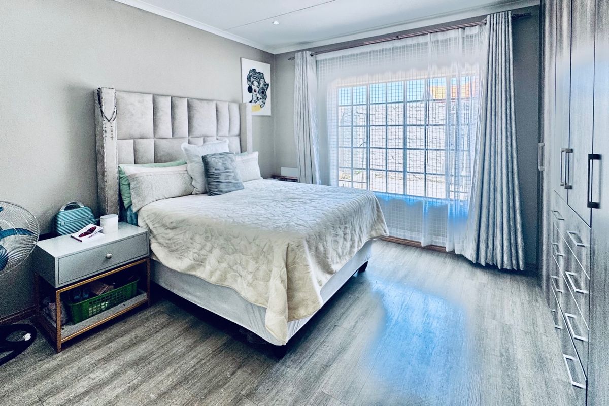 A well-maintained bedroom featuring modern laminate flooring, ample built-in cupboard storage, and large windows with curtain rails for natural light.