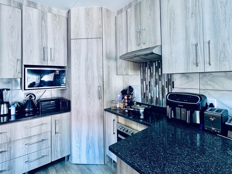 Modern kitchen featuring light wood-grain cabinetry, dark granite countertops, a tiled backsplash, and integrated appliances including an oven and extractor fan.