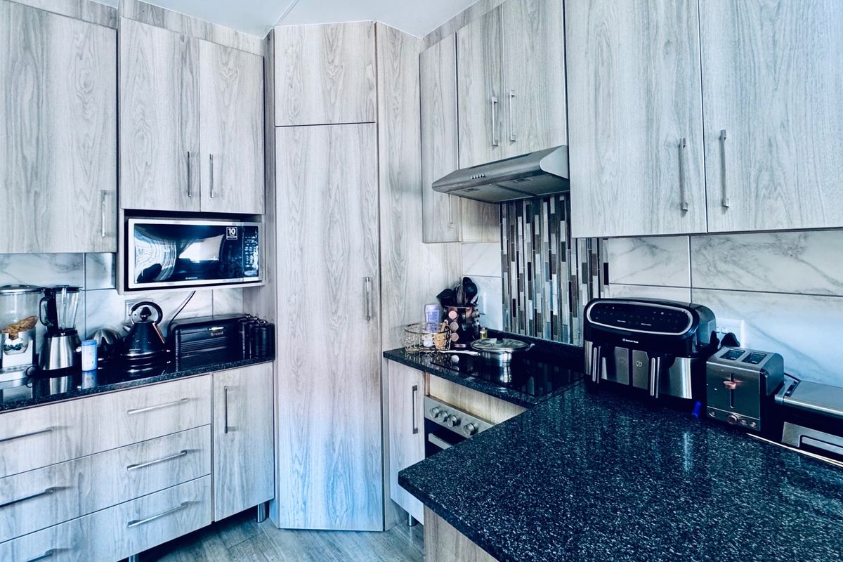 Modern kitchen featuring light wood-grain cabinetry, dark granite countertops, a tiled backsplash, and integrated appliances including an oven and extractor fan.