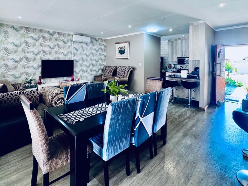 An open-plan living and dining area featuring laminate flooring, recessed lighting, and a modern kitchen with a breakfast bar and built-in appliances.