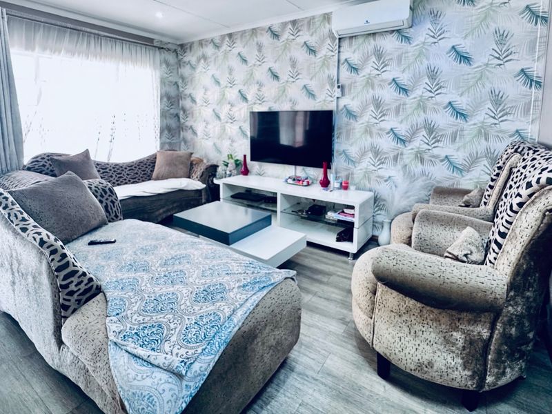 A living room featuring laminate flooring, patterned wallpaper, and a wall-mounted split-system air conditioner.