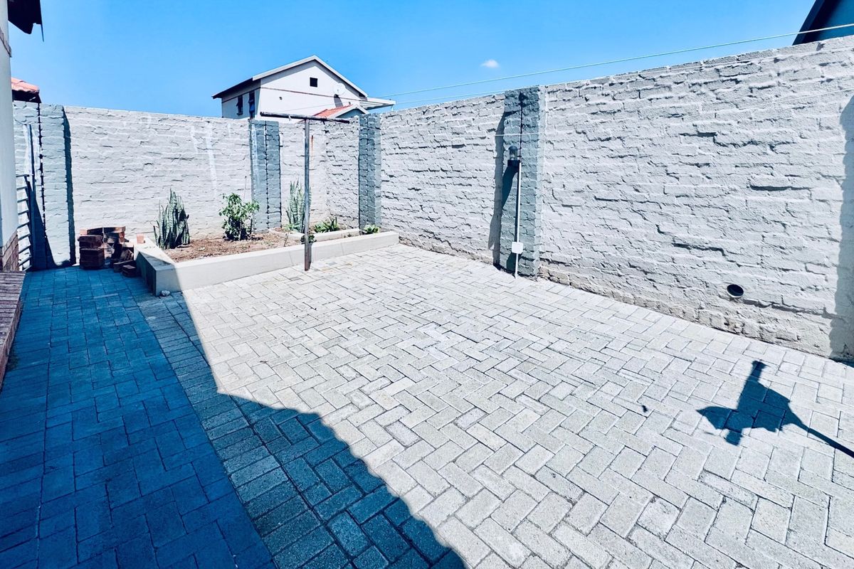 A private rear courtyard featuring paved flooring, a raised garden bed, and high brick boundary walls for added privacy.