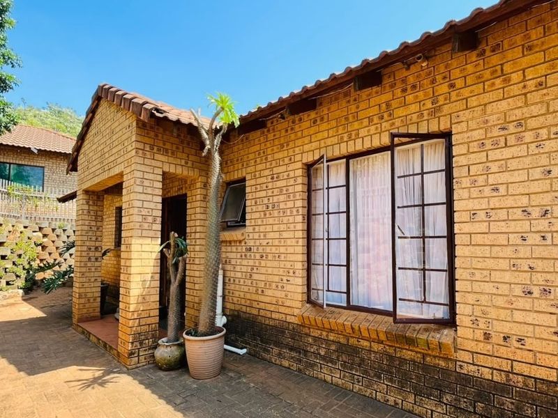 A rear view of a face brick house featuring a paved patio area, tiled roof, and casement windows with a retaining wall in the background.