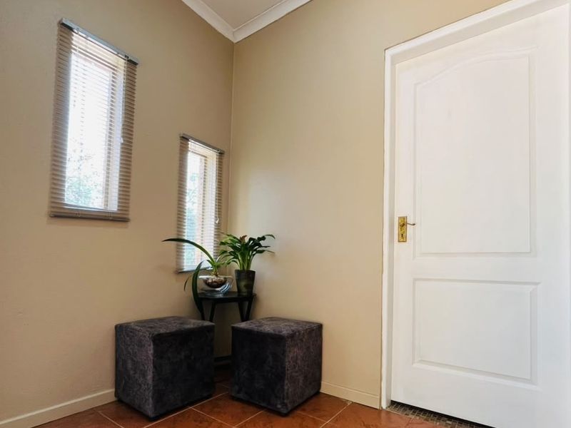 A bright entrance area featuring tiled flooring, a classic panelled door, and dual windows fitted with venetian blinds.
