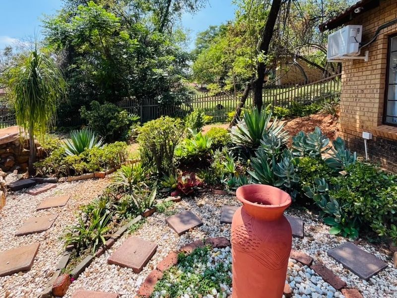 A well-maintained garden area featuring gravel pathways, stone retaining walls, and established succulent landscaping adjacent to the brick exterior of the house.
