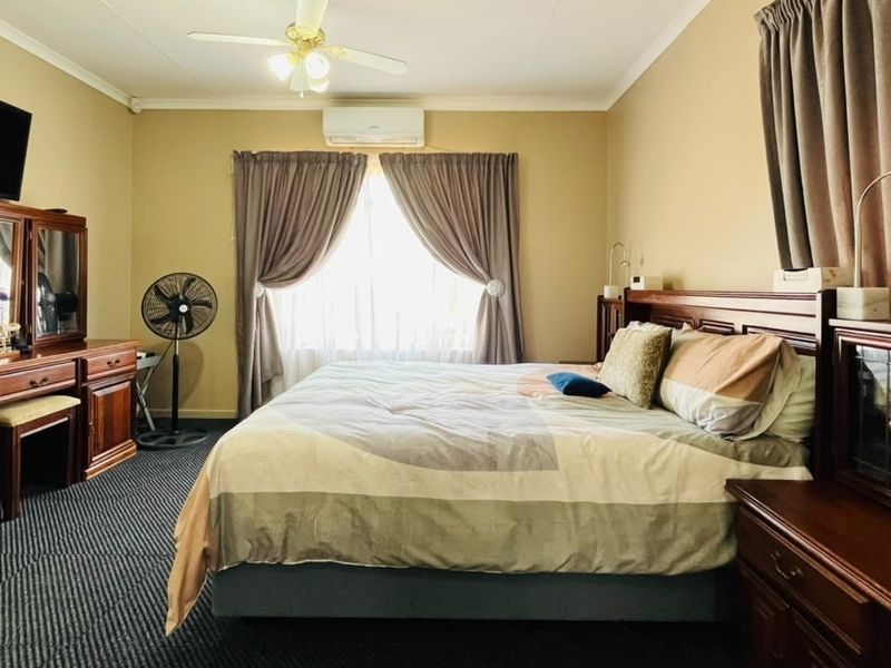A spacious bedroom featuring a ceiling fan, split-system air conditioning, and carpeted flooring, offering a comfortable and functional living space.