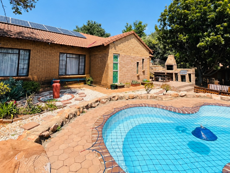 Rear exterior view featuring a swimming pool with safety net, brick braai area, and solar panels installed on the tiled roof.