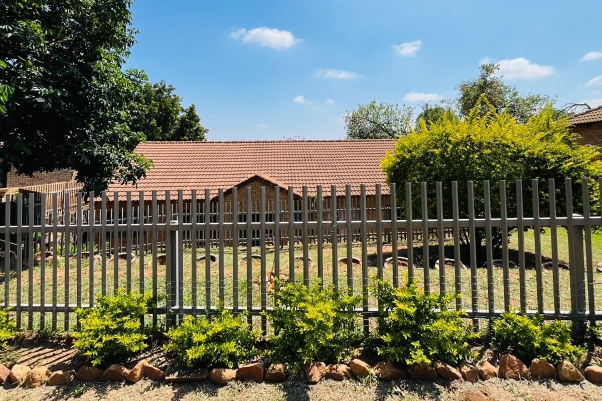 A view of the rear garden featuring a well-maintained lawn, mature shrubs, and secure steel palisade fencing against a brick house with a tiled roof.