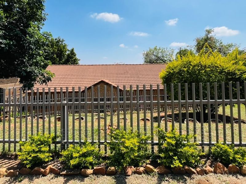 A view of the rear garden featuring a well-maintained lawn, mature shrubs, and secure steel palisade fencing against a brick house with a tiled roof.