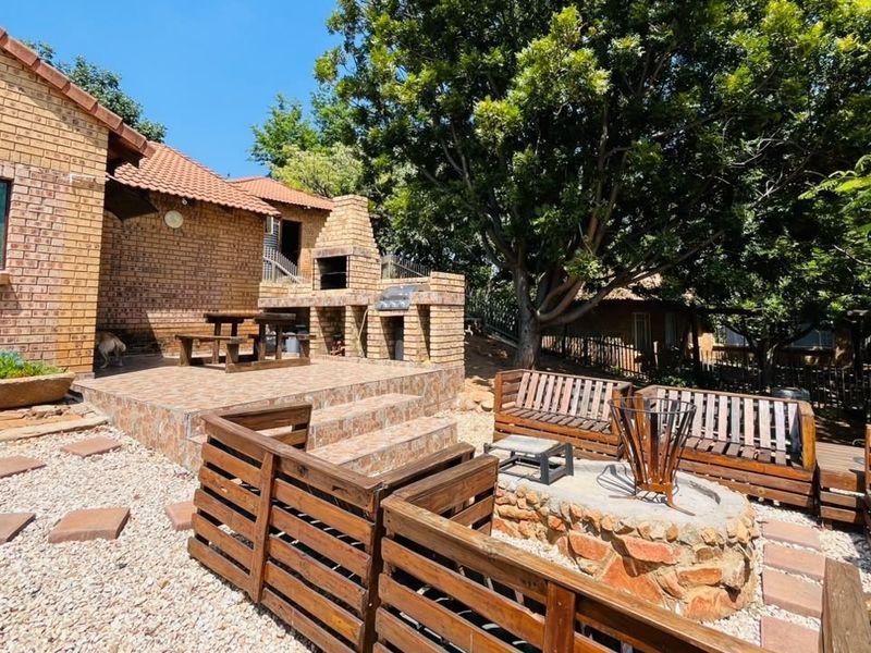 Outdoor entertainment area featuring a built-in brick braai, tiled patio, and a stone-clad fire pit set within a landscaped garden environment.