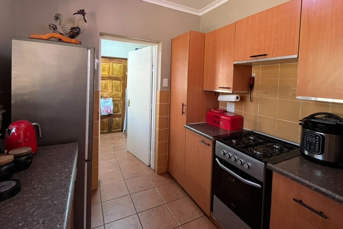 A functional kitchen featuring wooden cabinetry, tiled backsplash, gas stove, and oven, with tiled flooring and direct access to an adjacent room.