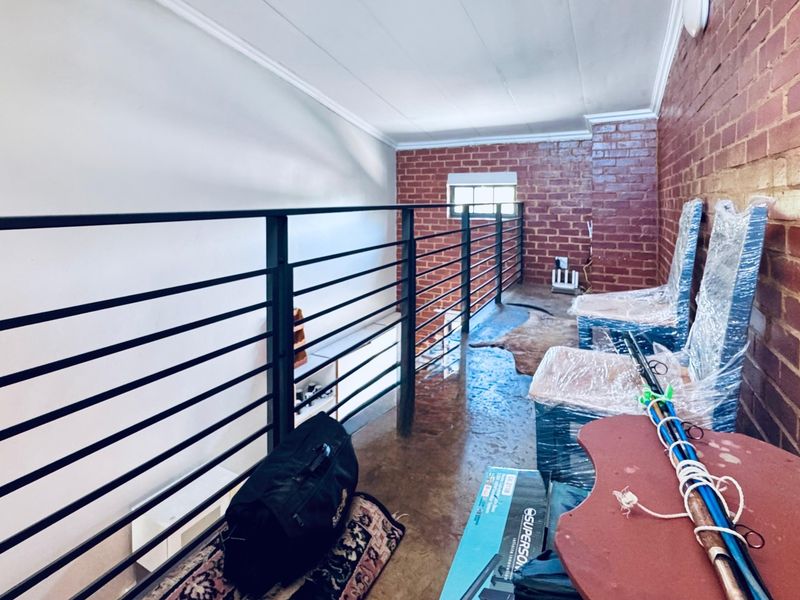 An elevated mezzanine hallway featuring exposed brick walls, concrete flooring, and a modern metal balustrade overlooking the lower level.