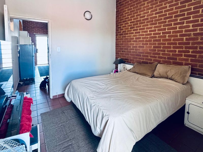 Bedroom featuring an exposed brick feature wall and tiled flooring, with direct access to an adjacent kitchen area.