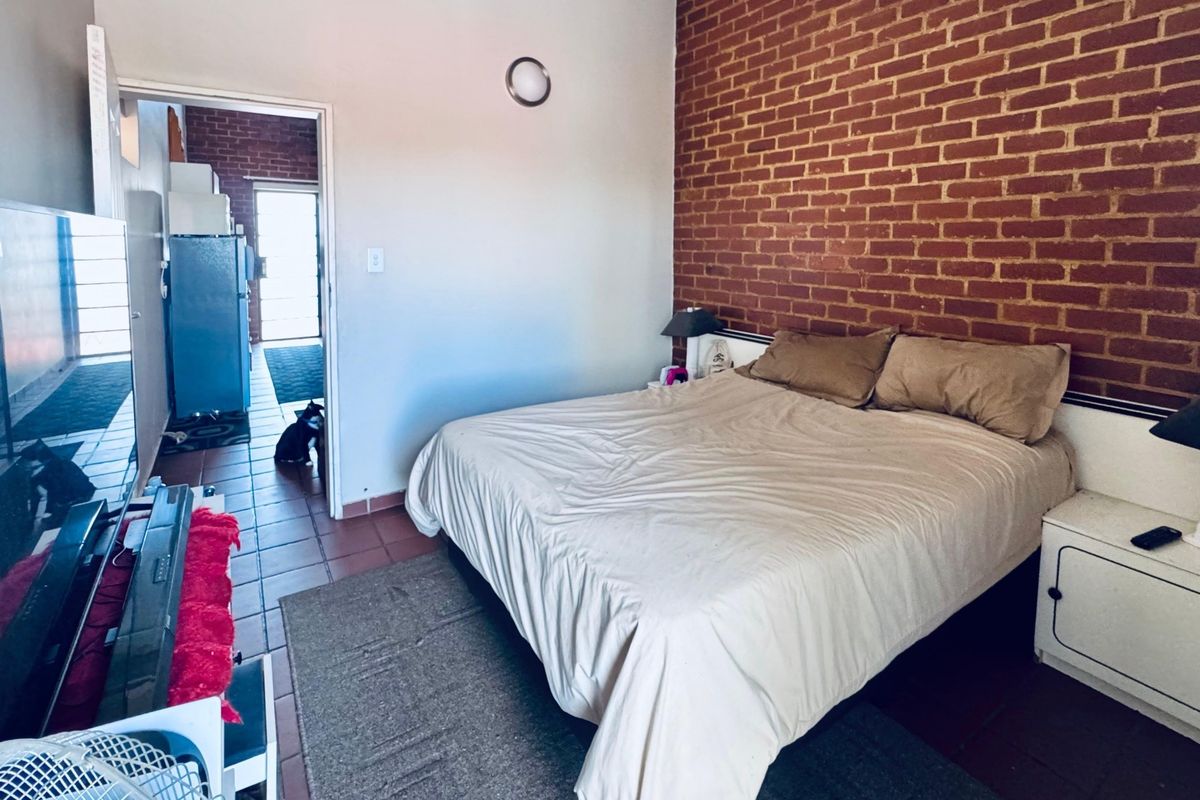 Bedroom featuring an exposed brick feature wall and tiled flooring, with direct access to an adjacent kitchen area.