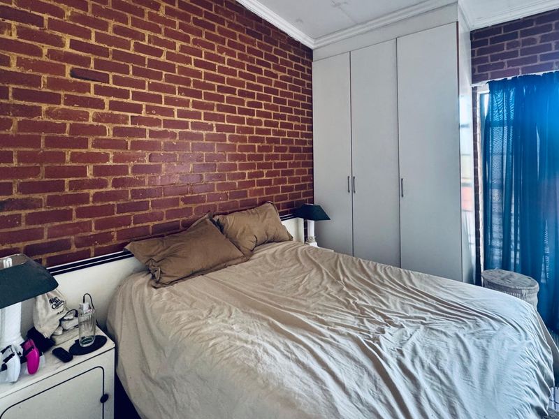 Bedroom featuring an exposed brick feature wall, built-in cupboards, and direct access to a balcony through a sliding door.