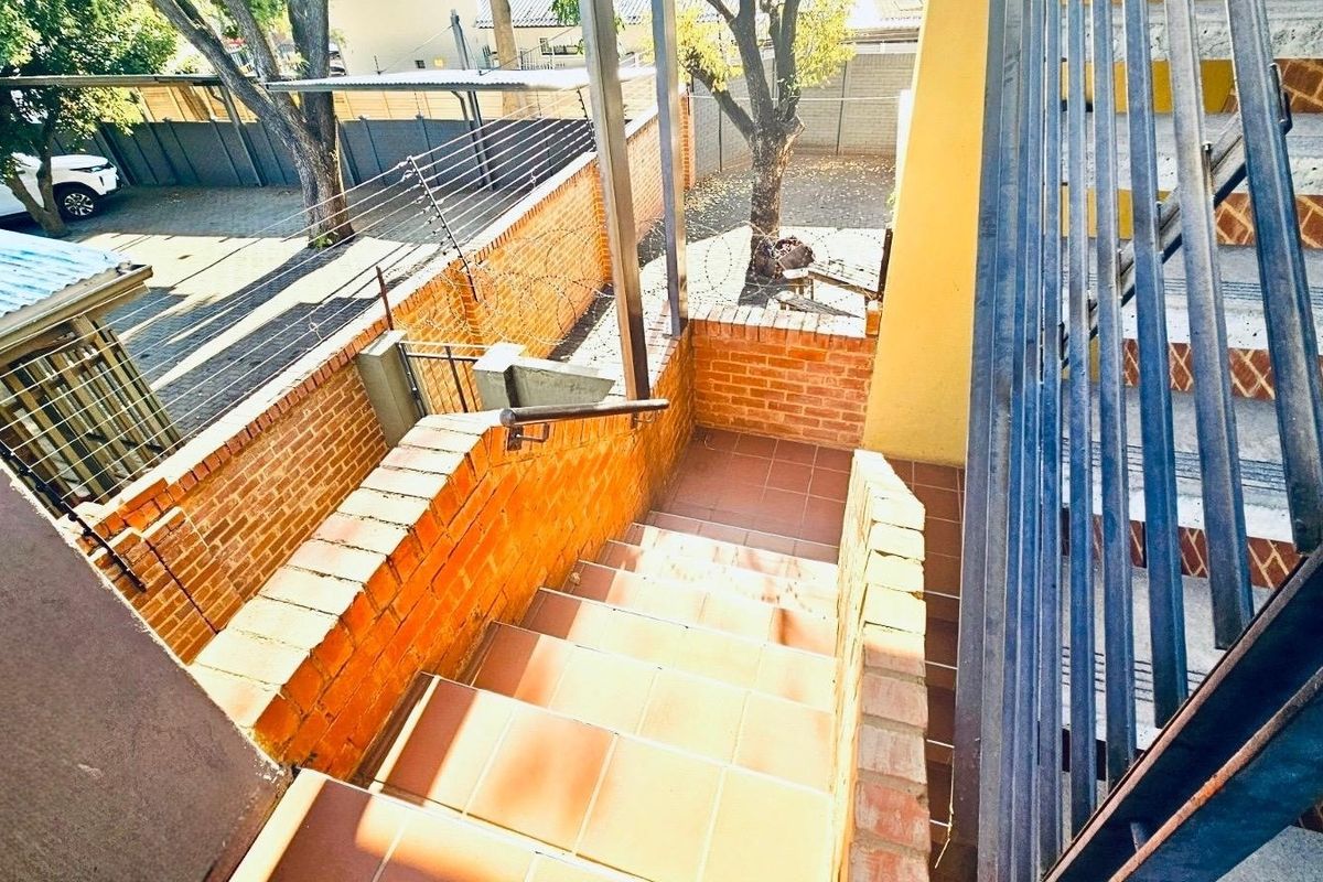 Exterior staircase with tiled steps and metal handrails, leading to a paved courtyard area enclosed by brick boundary walls and electric fencing.
