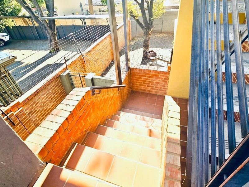 Exterior staircase with tiled steps and metal handrails, leading to a paved courtyard area enclosed by brick boundary walls and electric fencing.