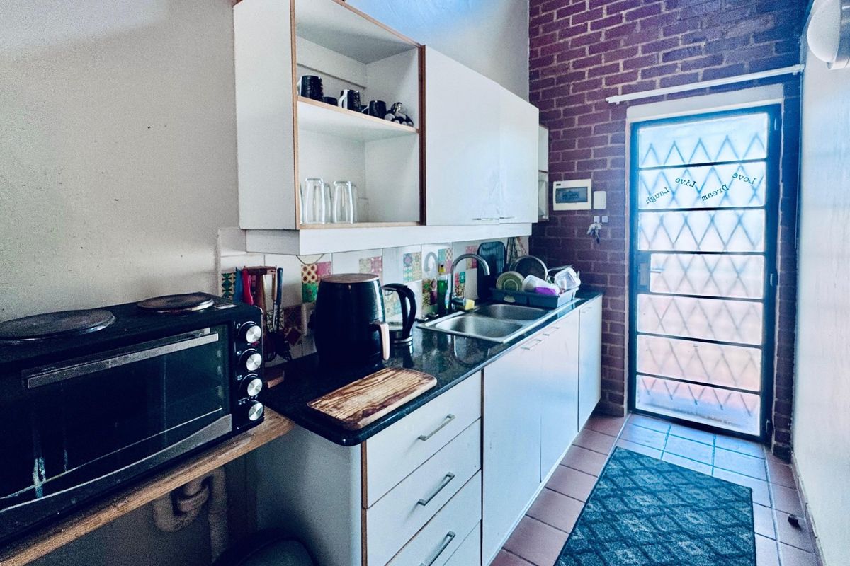 A functional kitchen featuring built-in cabinetry, a double bowl sink, and a distinctive exposed brick wall with direct access to an exterior door.