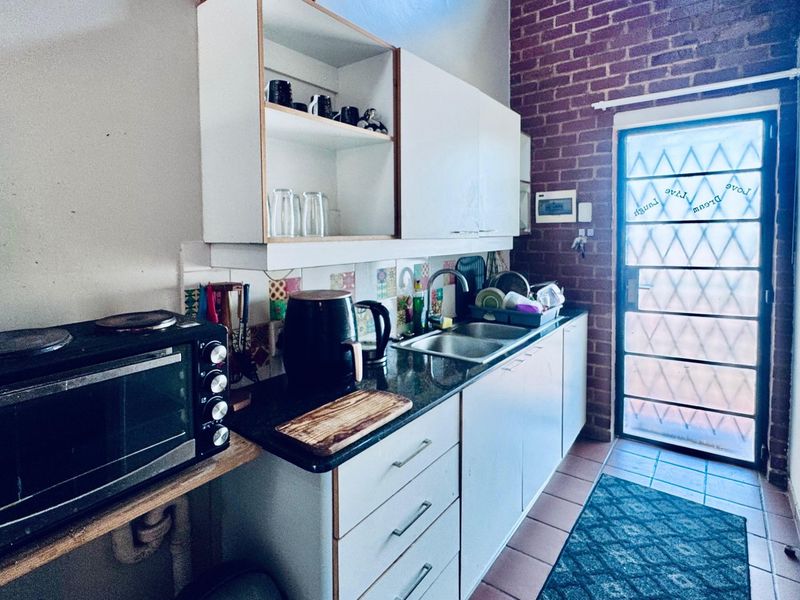A functional kitchen featuring built-in cabinetry, a double bowl sink, and a distinctive exposed brick wall with direct access to an exterior door.