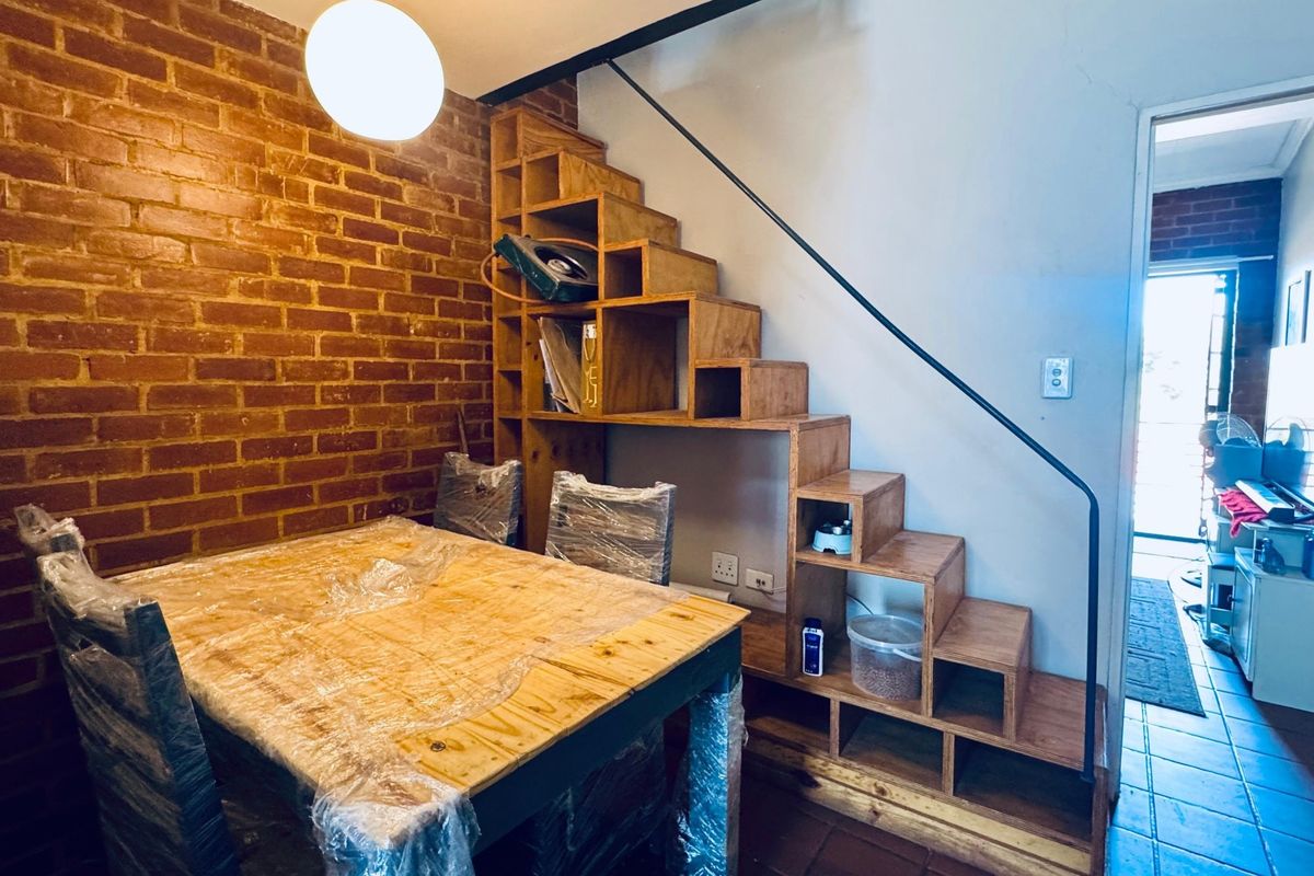Living area featuring an exposed brick wall and a unique built-in wooden staircase with integrated shelving, leading to an upper level.