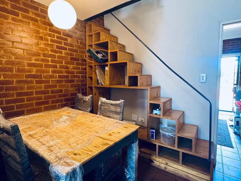 Living area featuring an exposed brick wall and a unique built-in wooden staircase with integrated shelving, leading to an upper level.
