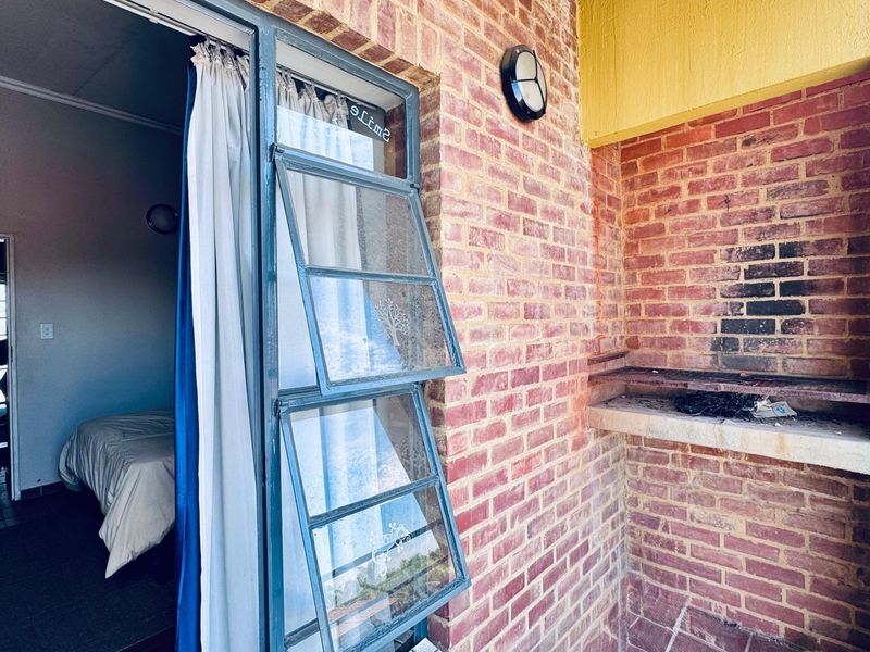 A balcony area featuring an exposed brick wall with a built-in braai and direct access to the interior living space.