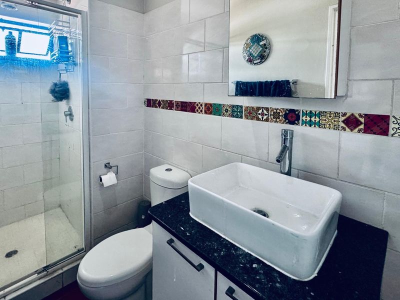 A functional bathroom featuring a glass shower enclosure, a modern vessel sink on a granite vanity, and decorative tiled wall accents.