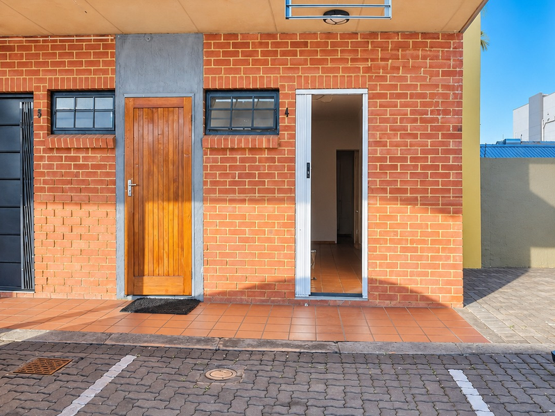 Front exterior view of an apartment unit featuring a brick facade, tiled porch area, and secure access points with paved driveway parking.