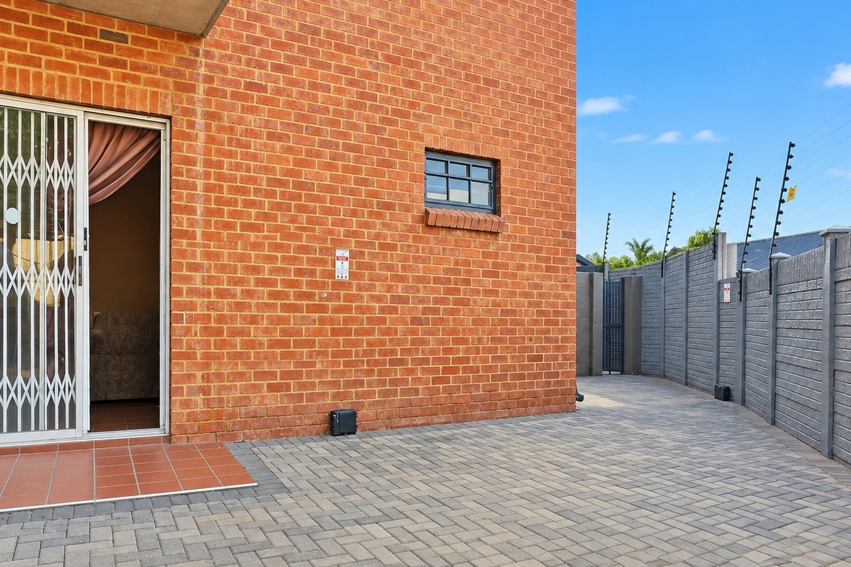 Rear exterior view featuring a brick facade, paved patio area, and secure boundary wall with electric fencing.