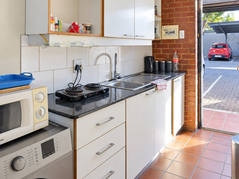 Compact kitchen featuring white cabinetry, granite countertops, tiled backsplash, and direct access to the exterior parking area.