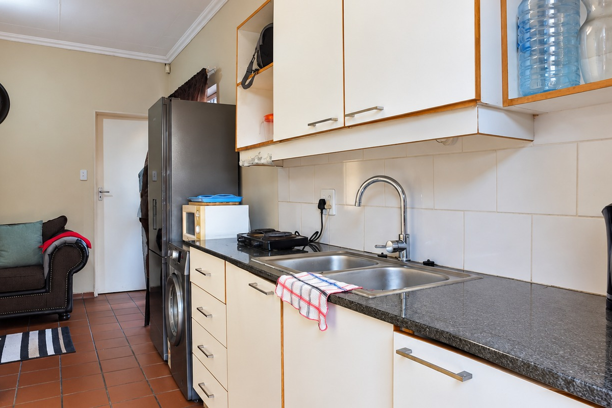 Compact kitchen featuring built-in cabinetry, granite countertops, a double bowl stainless steel sink, and tiled backsplash, with adjacent tiled flooring.