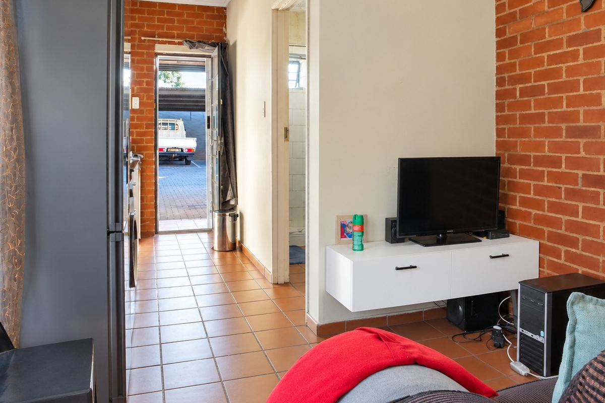Living area featuring exposed brick walls and ceramic floor tiles, with direct access to an exterior parking area.