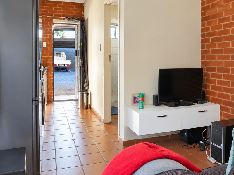 Living area featuring exposed brick walls and ceramic floor tiles, with direct access to an exterior parking area.