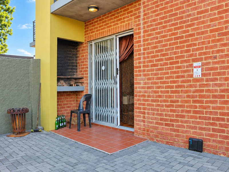 A private ground-floor patio featuring a built-in braai, tiled flooring, and a secure sliding door entrance to the apartment.