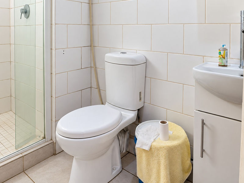 Compact bathroom featuring a shower enclosure, white toilet, and a small vanity basin with tiled wall and floor finishes.