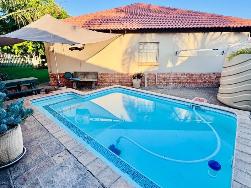 Outdoor pool area featuring a swimming pool with tiled surround, shade sail, and a water storage tank set against the rear building elevation.
