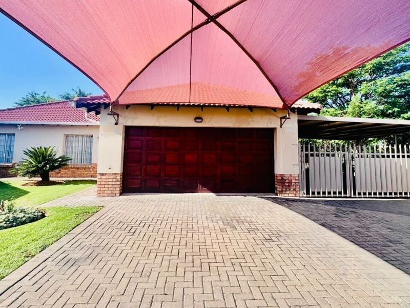Front exterior view featuring a paved driveway, a large pink shade sail, and a secure garage entrance with a tiled roof.