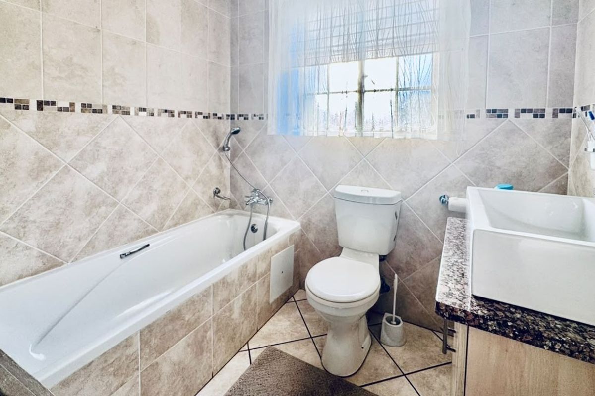 A functional bathroom featuring a built-in bathtub, toilet, and a vanity basin with a granite countertop, finished with neutral wall and floor tiling.