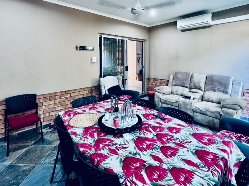 Covered patio area featuring tiled flooring, brick wall accents, a built-in fireplace, and a wall-mounted air conditioning unit.