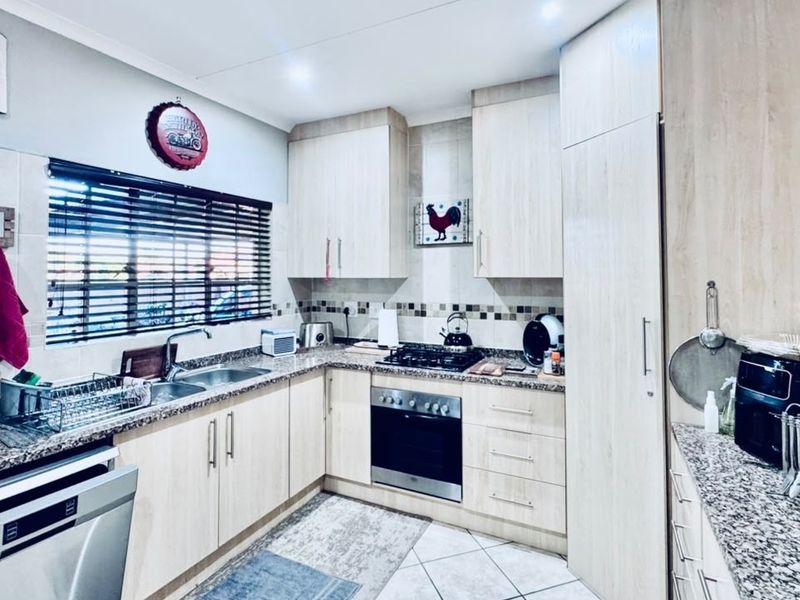 A functional kitchen featuring light wood-finish cabinetry, granite countertops, a built-in oven with gas hob, and tiled flooring.