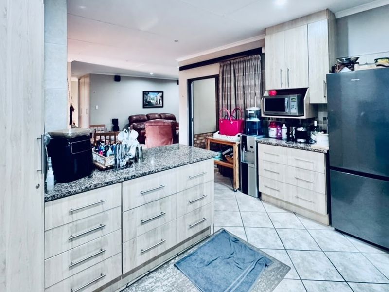 Open-plan kitchen featuring light wood-finish cabinetry, granite countertops, and tiled flooring, seamlessly flowing into the adjacent living area.
