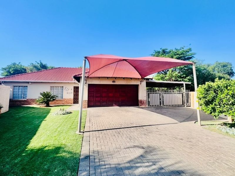 Front view of a well-maintained house featuring a paved driveway, double garage with a shade sail, and a neat front lawn.