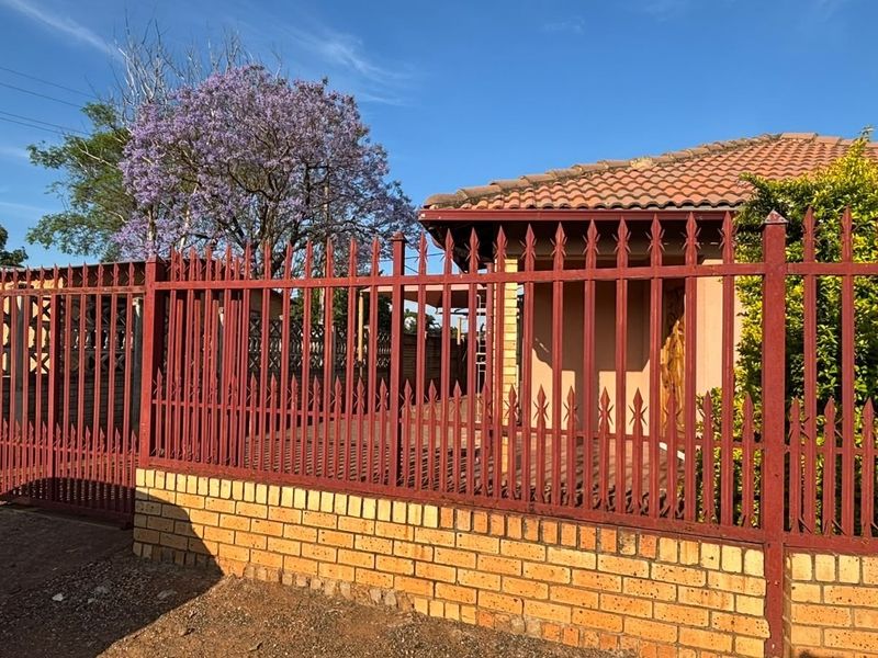 Front view of the property featuring a secure brick and metal picket fence, tiled roof, and gated entrance.