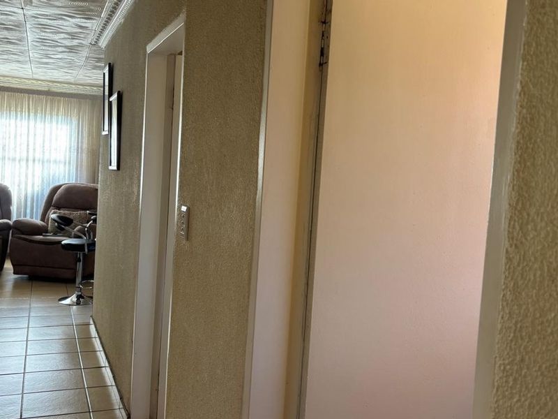 A narrow hallway featuring tiled flooring, textured walls, and decorative ceiling tiles, providing access to adjacent rooms.