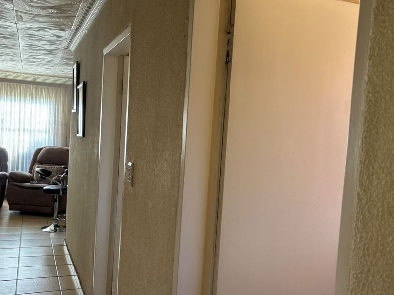 A narrow hallway featuring textured walls, tiled flooring, and decorative ceiling tiles, providing access to adjacent rooms.