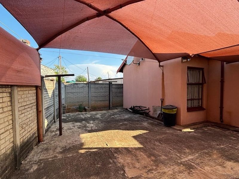 A paved outdoor patio area featuring a large overhead shade sail and enclosed by perimeter brick walls.